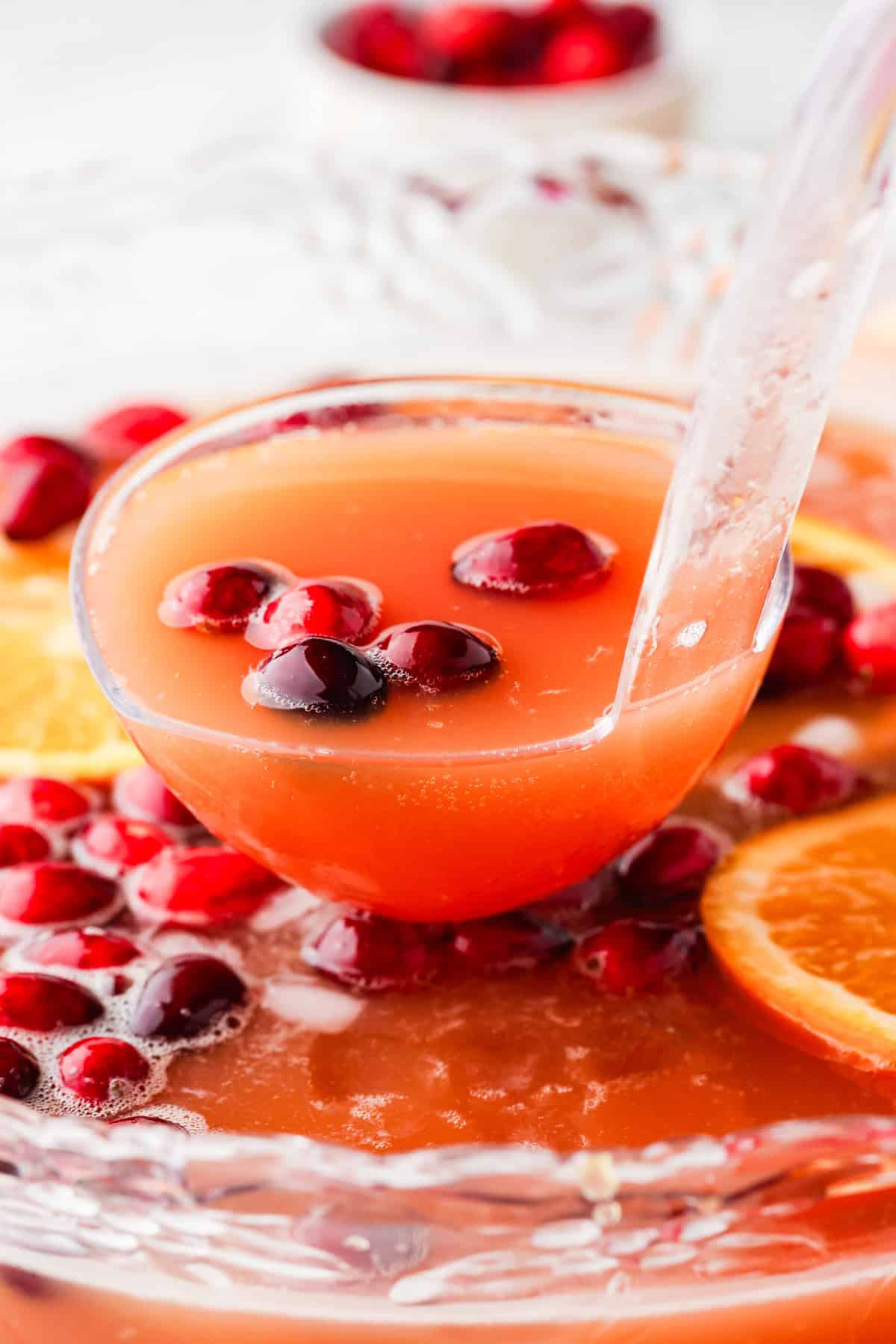 Ladle holding up punch, hovering over a punch bowl filled with punch and cranberries.