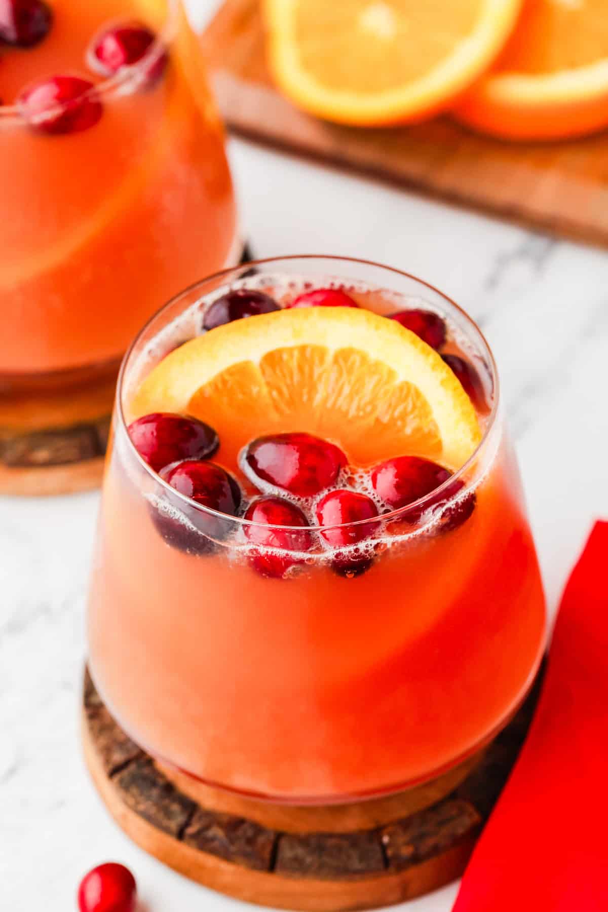 Glasses of festive punch, with cranberries and an orange slice floating on top.