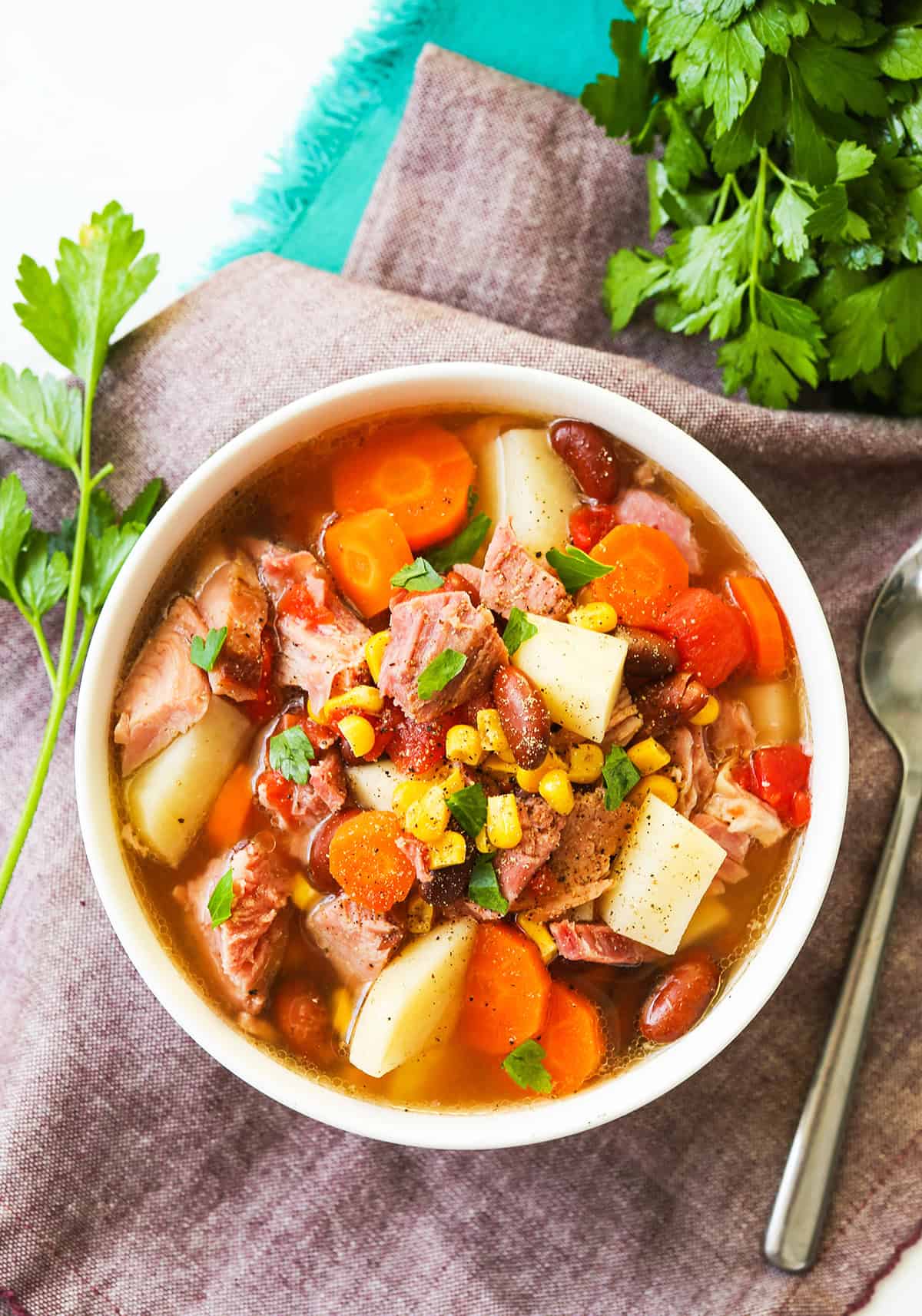 Bowl of ham bone soup loaded with veggies, next to parsley and a spoon.