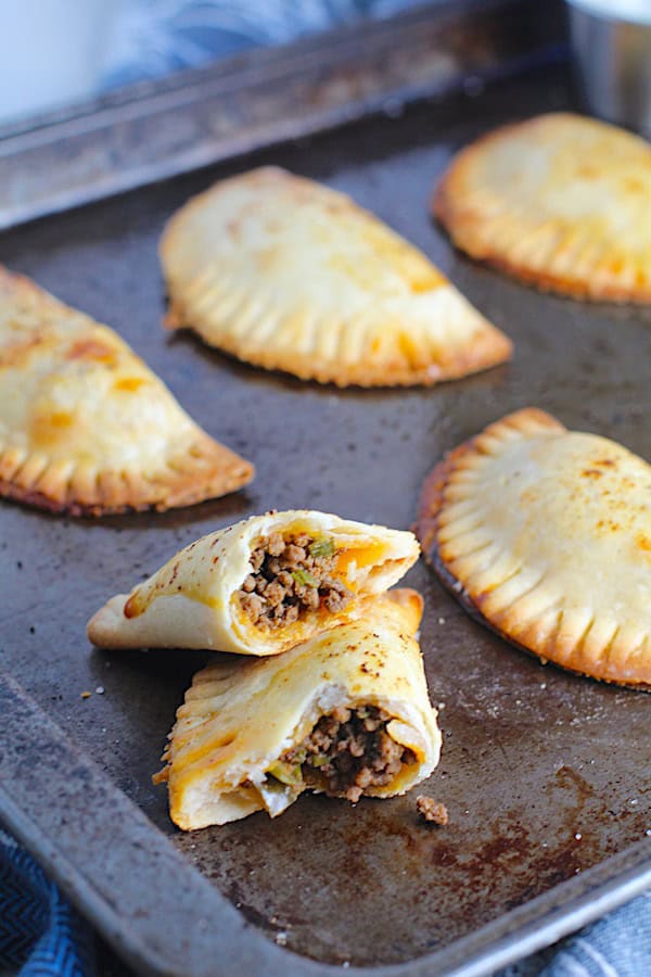 A spiced beef empanada broken in ahlf on a baking sheet. 