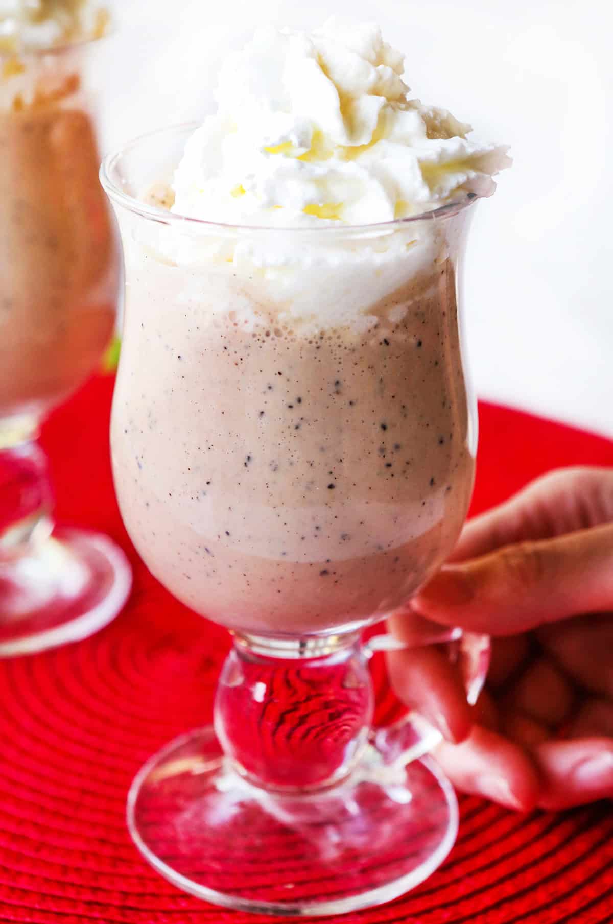 Hand holding handle of a glass filled with baileys Irish cream topped with whipped cream.