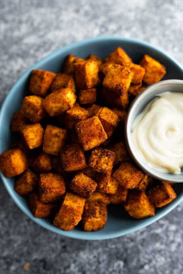 Air fryer tofu in a bowl with a side of sauce. 