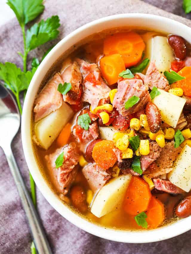 Ham bone bean soup with potatoes in a bowl and a spoon laying next to it. 