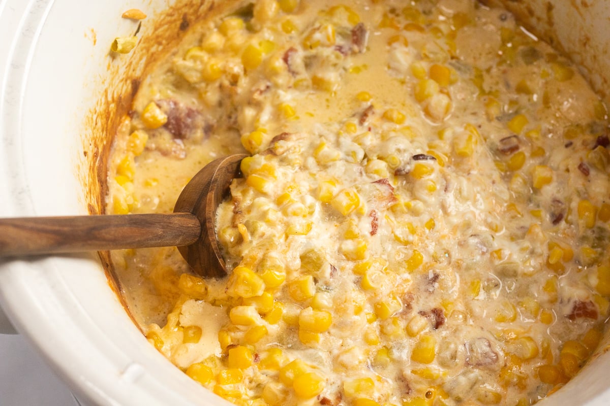Wooden spoon sticking into a crockpot filled with cheesy corn dip.
