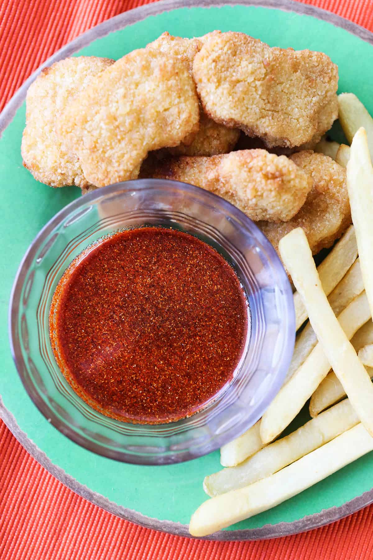 Sauce that looks really spicy in a small bowl, on a plate with chicken nuggets and fries.