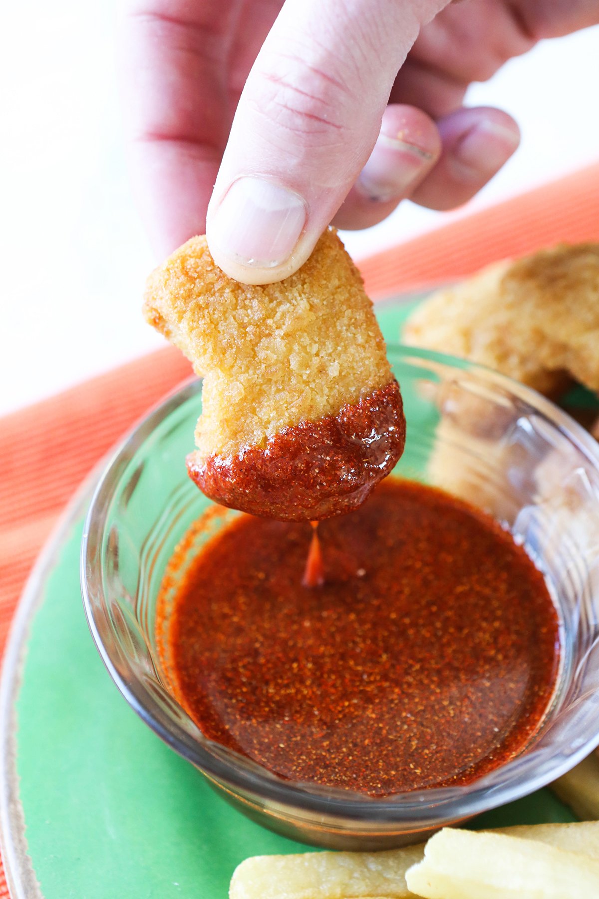 Fingers dipping a chicken nugget into sweet heat sauce.