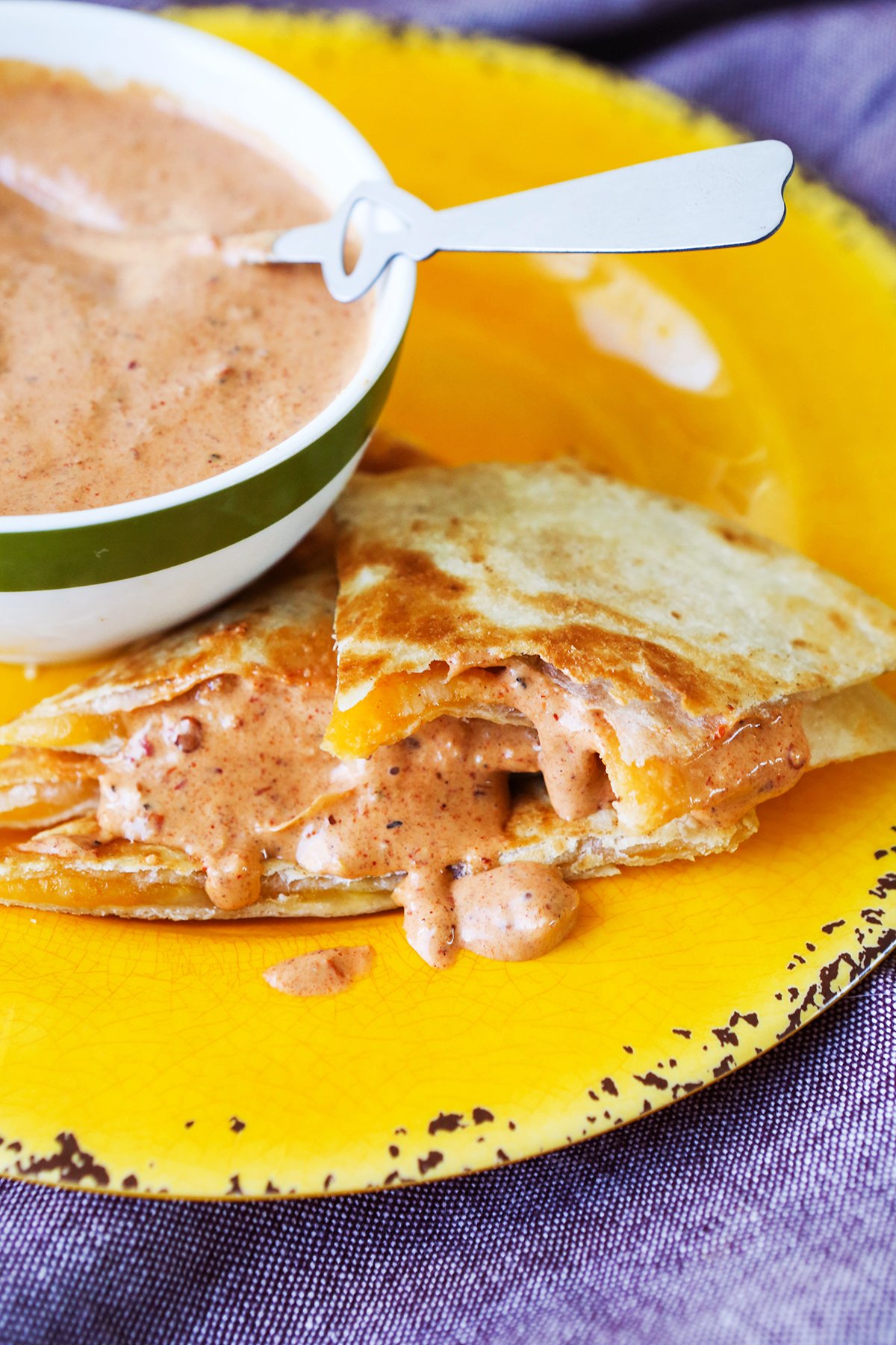 Cheese quesadillas stacked on a plate with chipotle sauce running out sides.