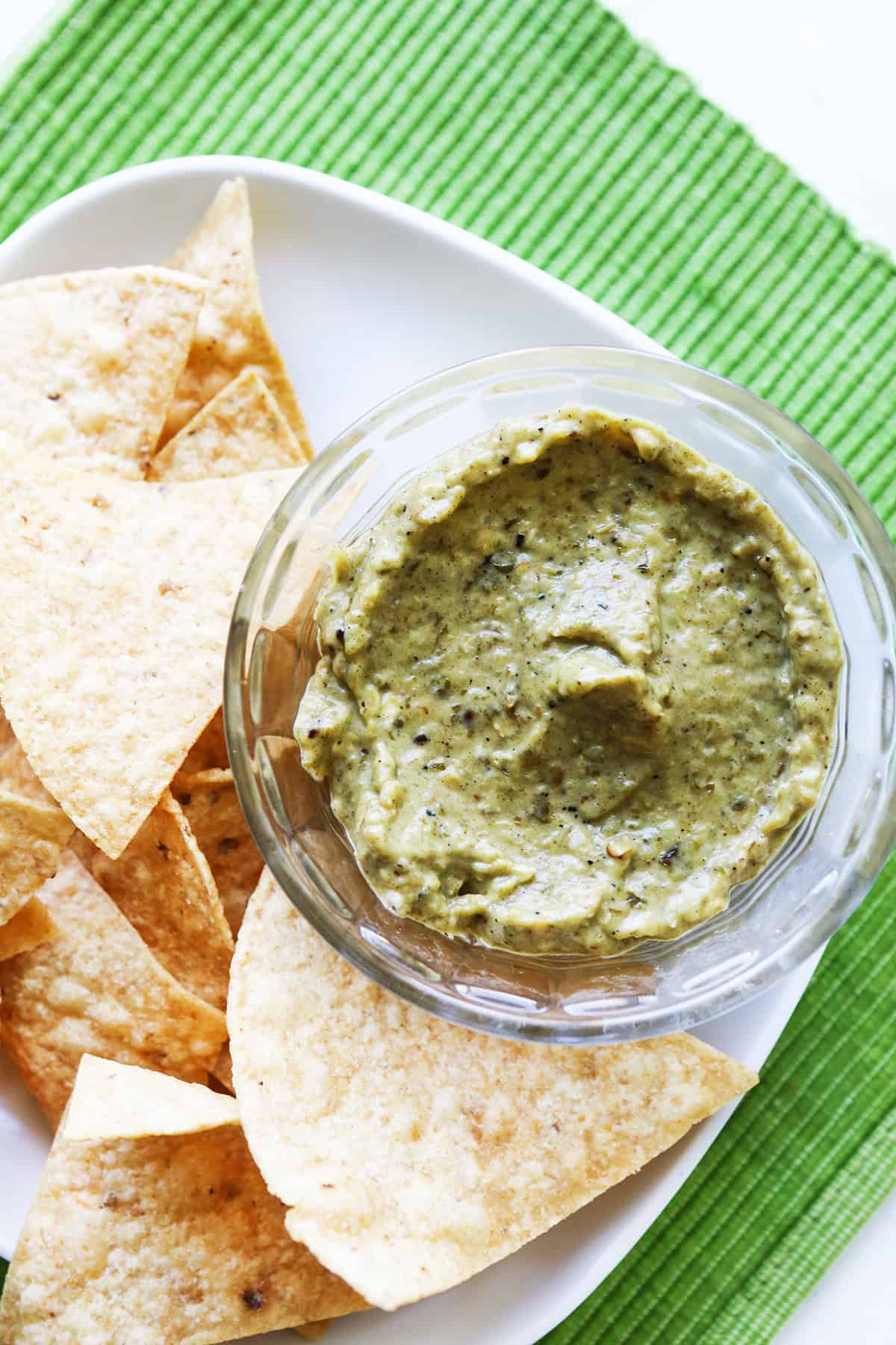 Top view of a small bowl of taco truck green sauce surrounded by tortilla chips.