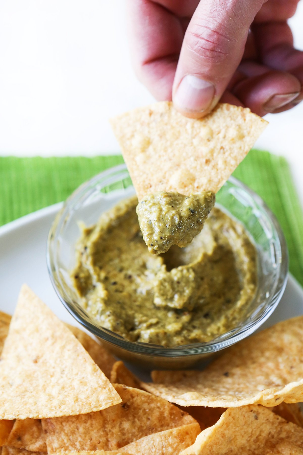 Fingers holding tortilla chip that has been dipped in green sauce.