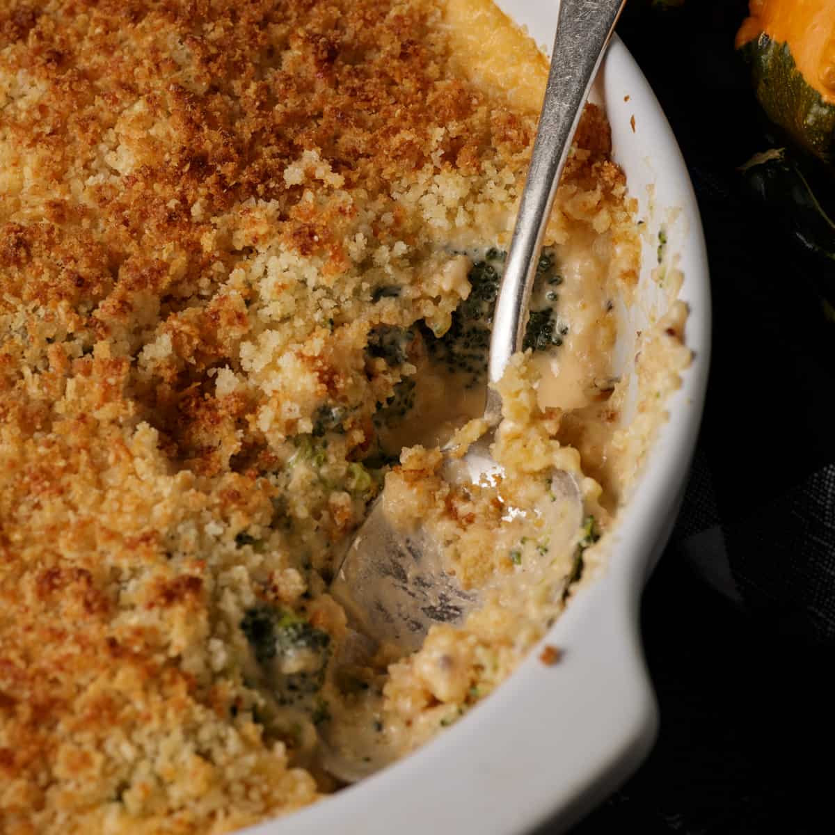 Spoon tucked into a baking dish of broccoli cheese casserole. 