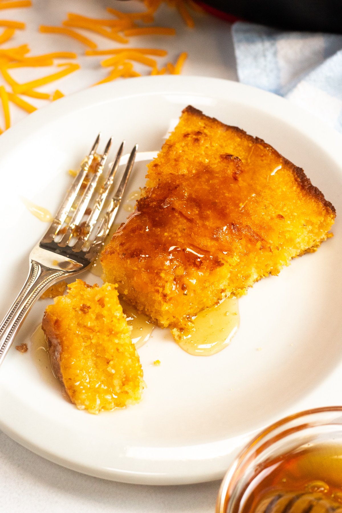 Slice of cornbread on a plate with honey drizzled over top.