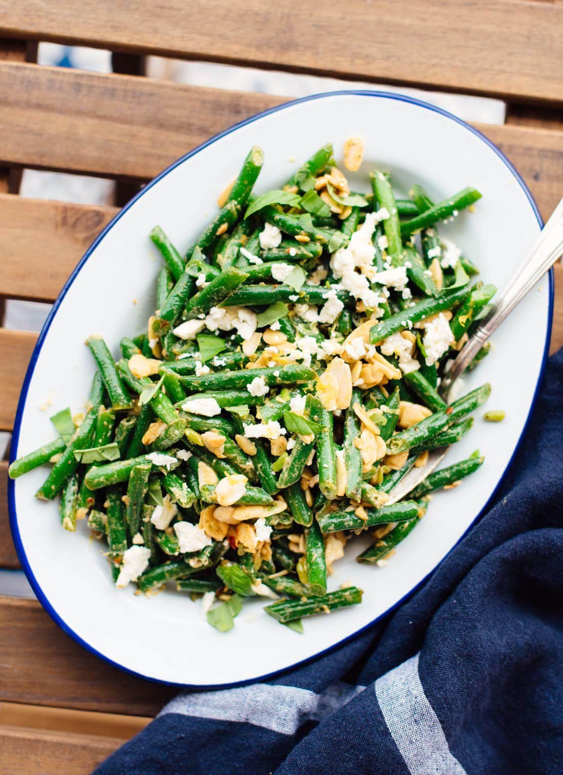 Oval serving platter with green bean salad with almonds and feta cheese. 
