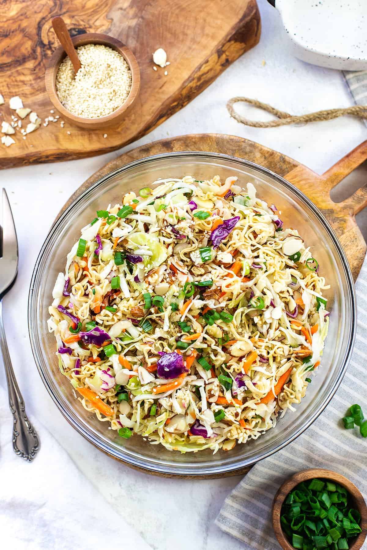 ramen noodle salad in a glass bowl sitting on a cutting board. 