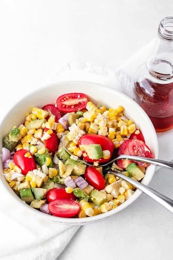 A spoon tucked inside Avocado Corn Salad with white balsamic honey reduction dressing on the side. 
