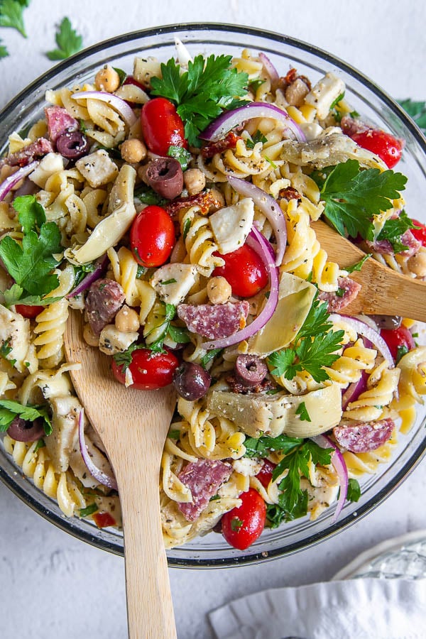 Wooden salad tongs in a bowl of sun dried tomato pasta salad. 