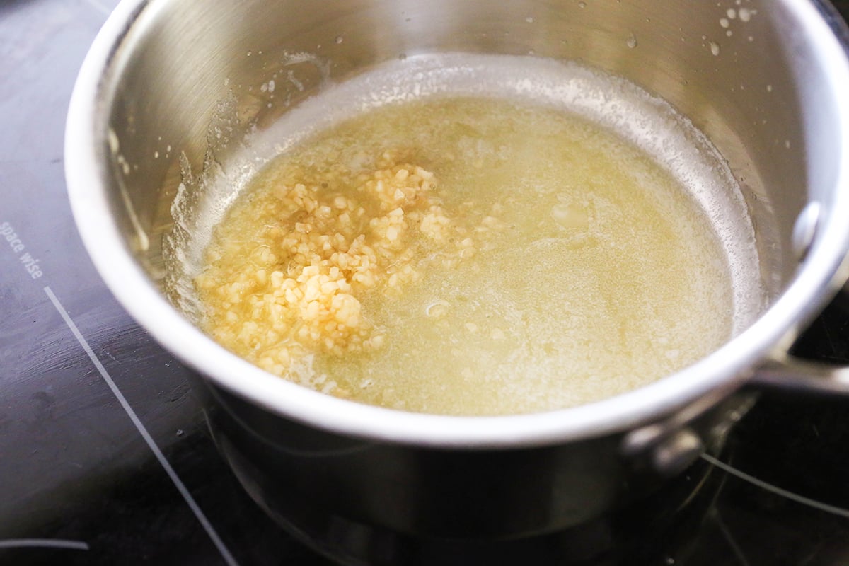 Garlic cooking in butter inside a saucepan.