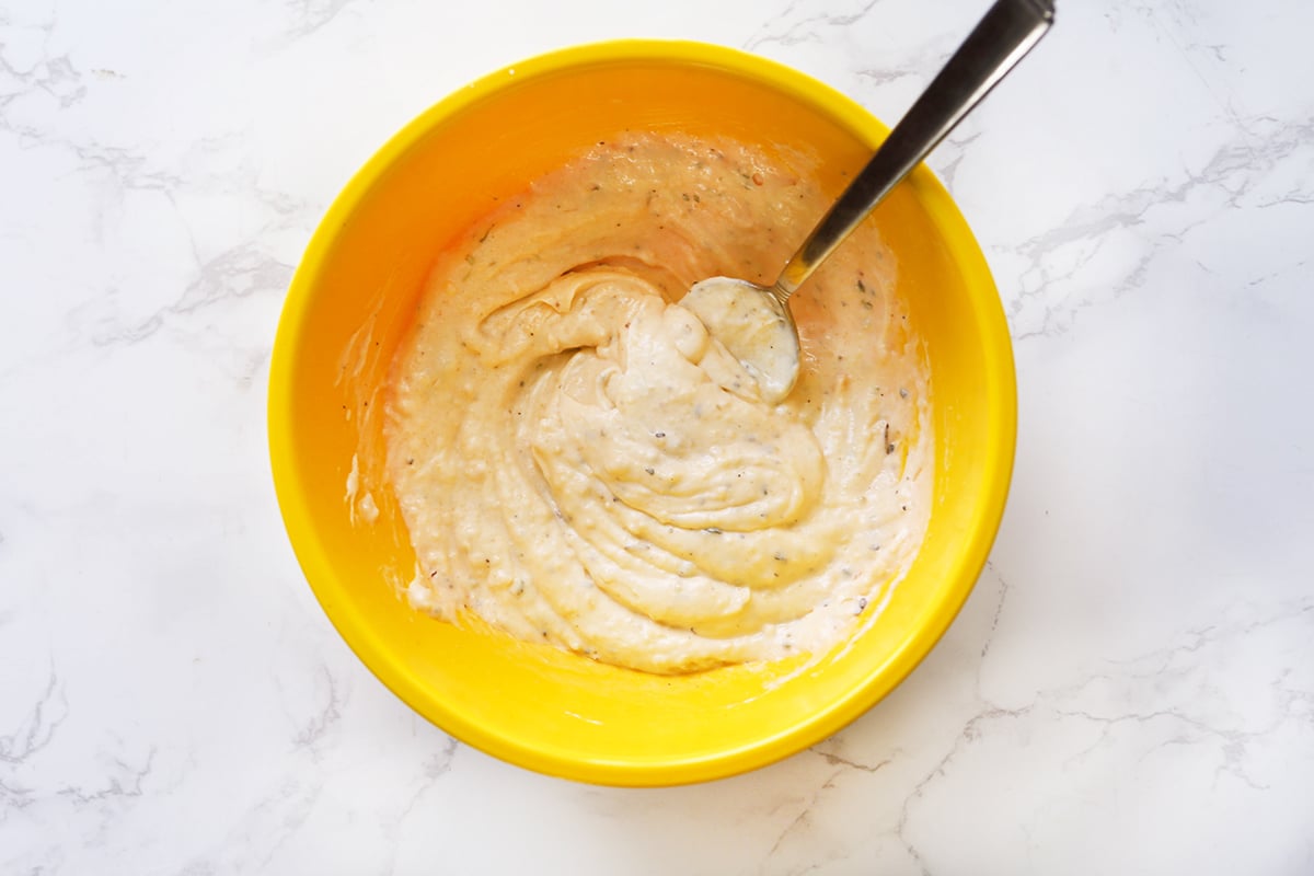 Spoon inside a bowl with a mixture of mayo-based sauce.
