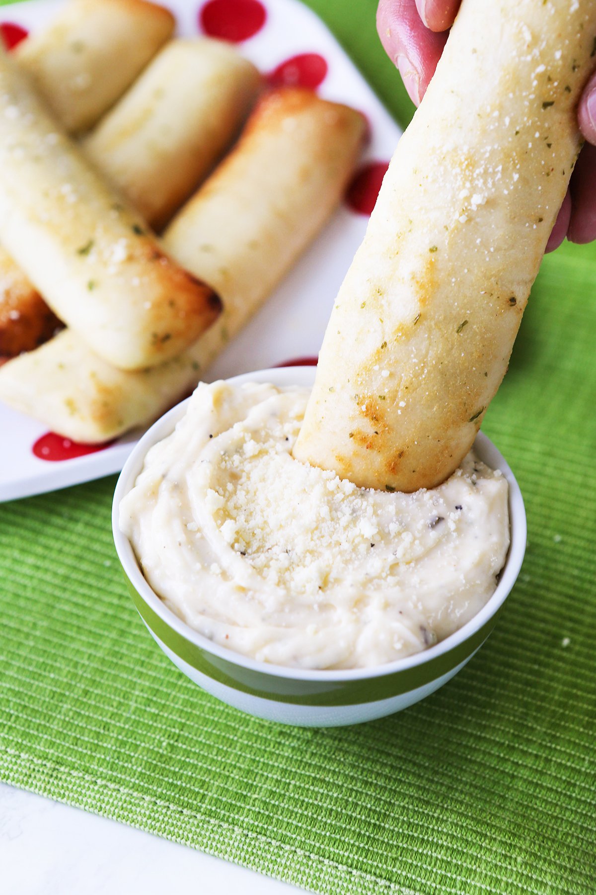 Breadstick being dipped into a bowl of creamy white sauce.