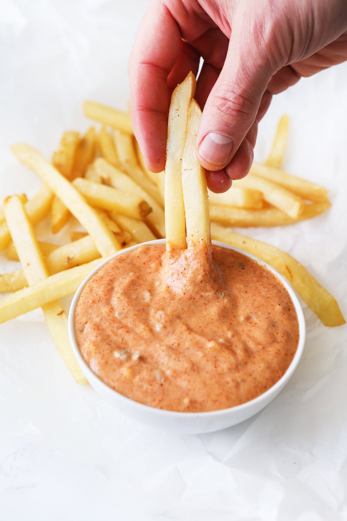 Hand dipping two fries into a bowl of sauce.