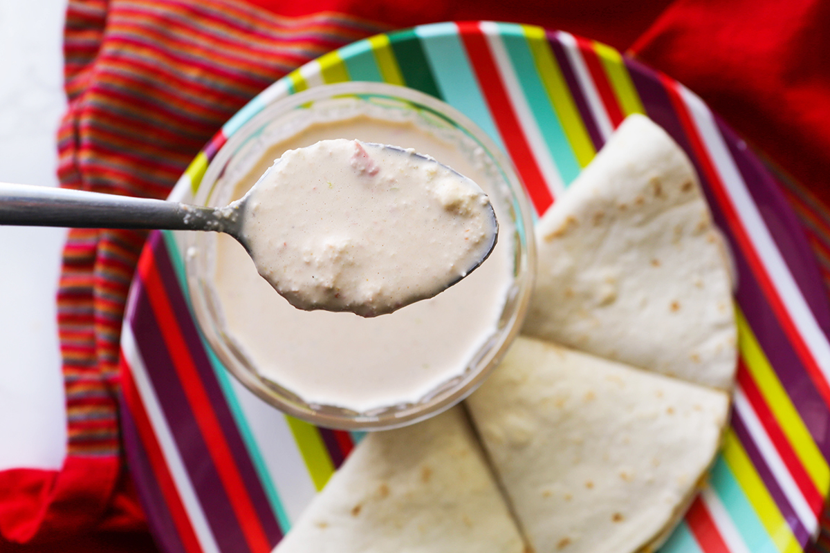 Chunky white baja sauce being spooned out of a bowl, next to quesadillas.