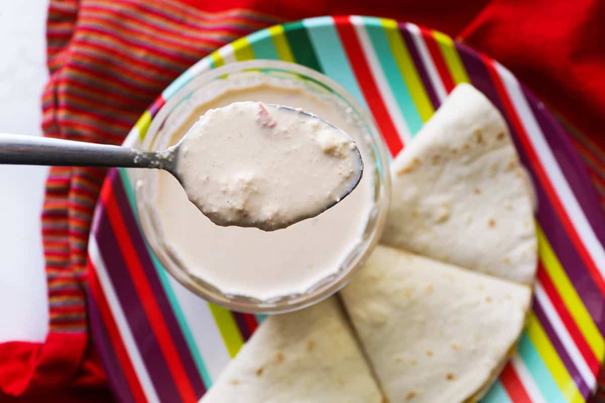 Spoon holding sauce over plate of quesadillas.