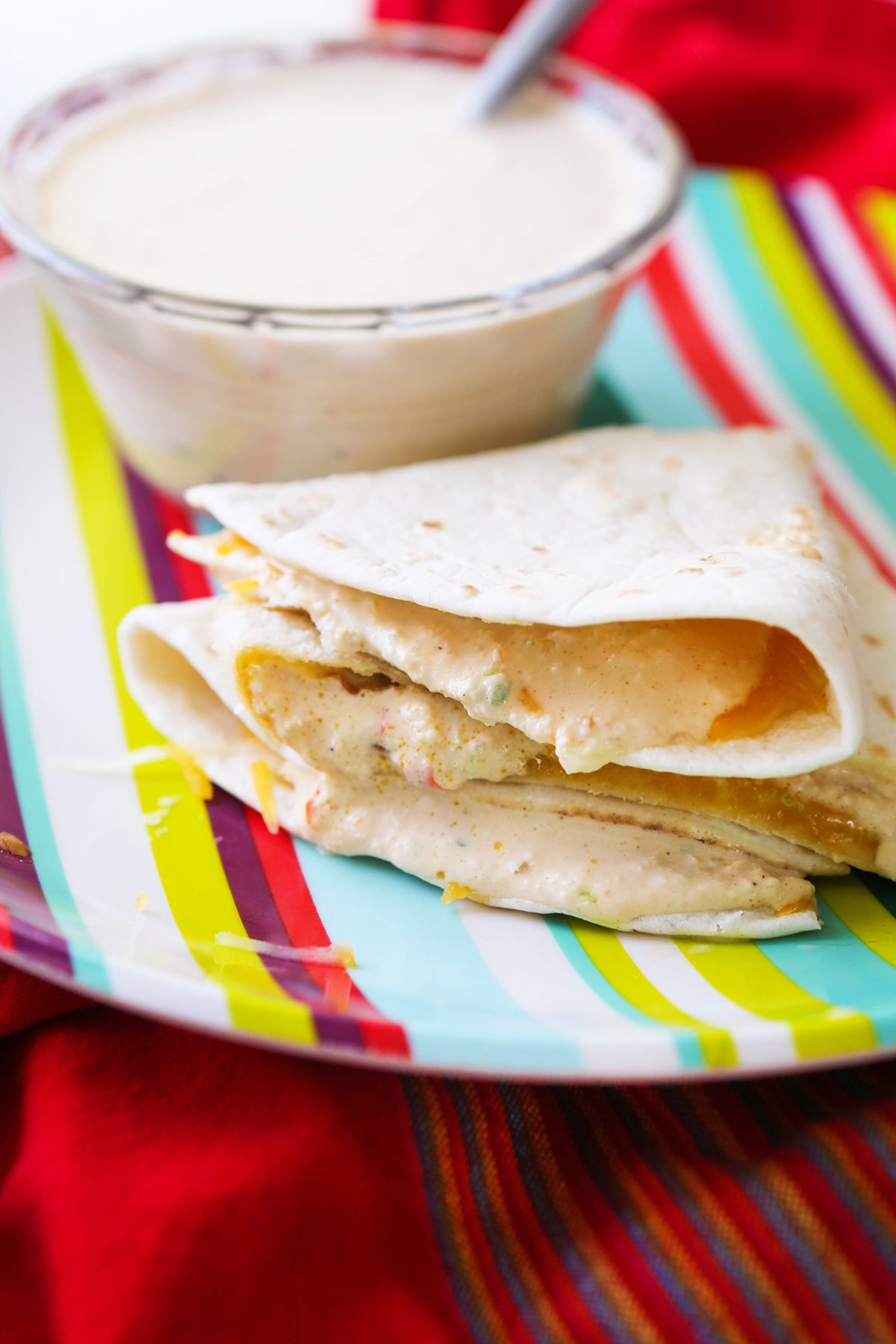 Quesadillas stacked on a plate with baja sauce dripping out sides.