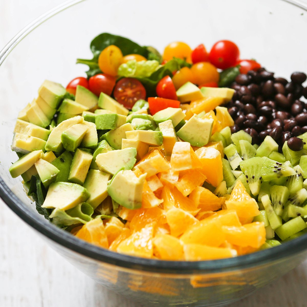 Chopped avocados, oranges, tomatoes and black beans in a bowl.