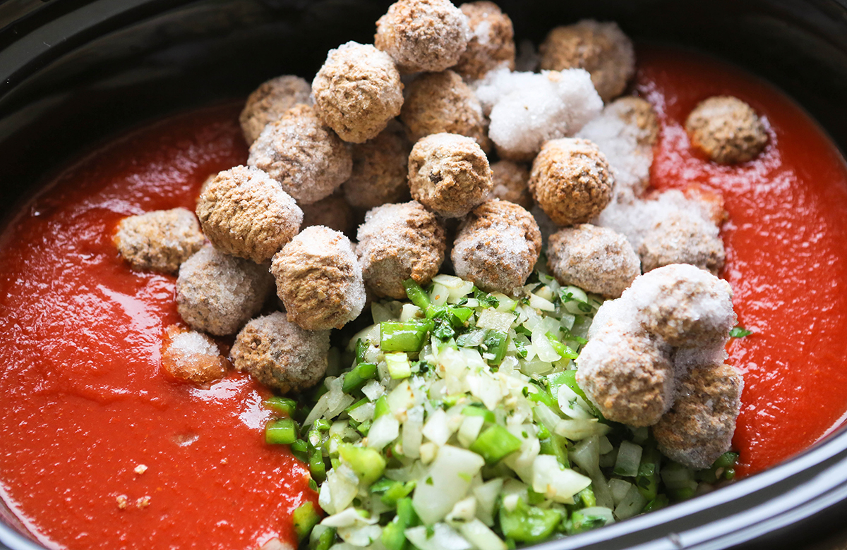 Pasta sauce in a slow cooker, topped with frozen meatballs and onion pepper mixture.