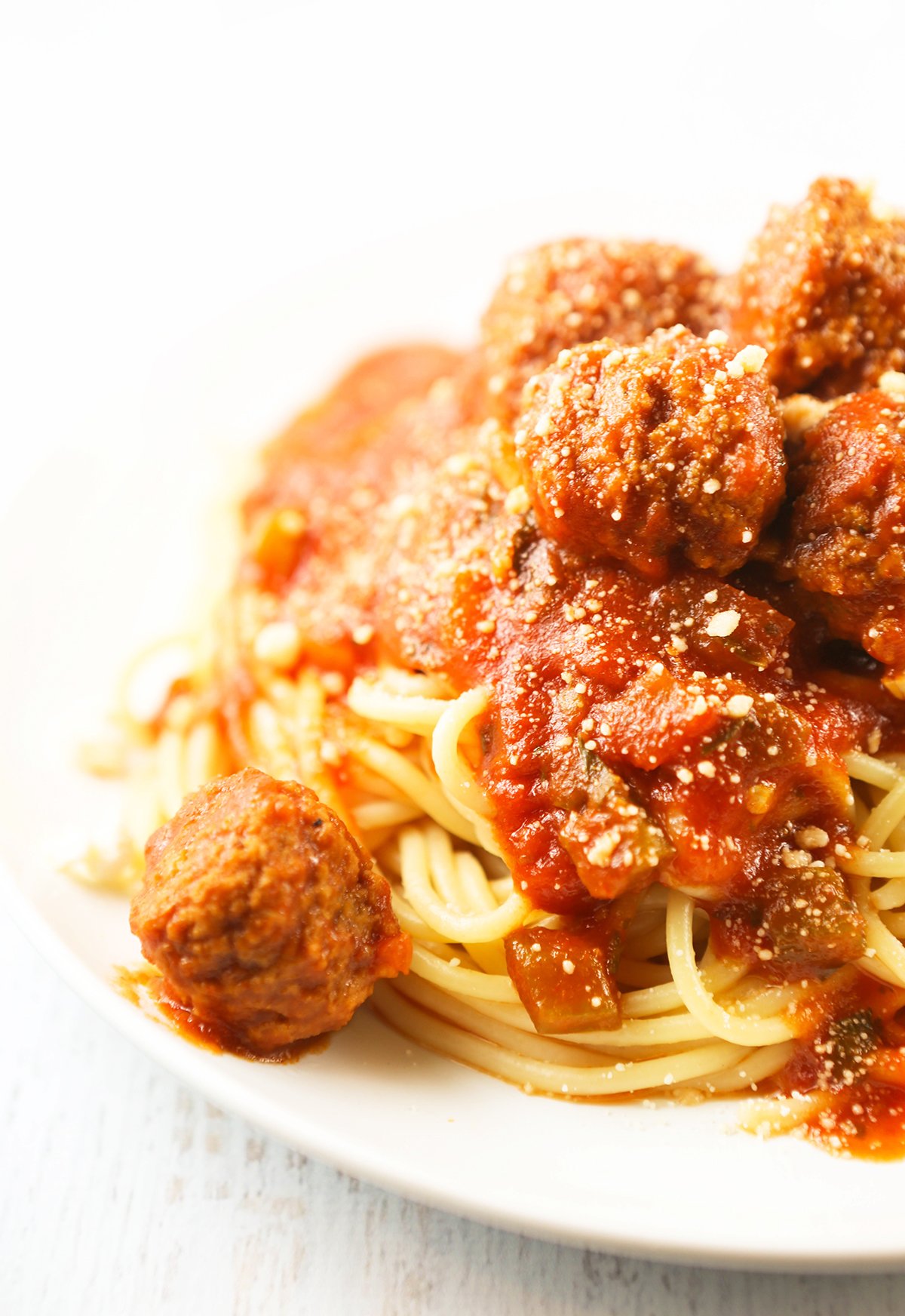 Huge pile of spaghetti and meatballs on a plate, topped with grated parmesan cheese.