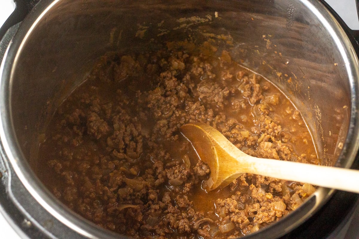 Cooked sloppy joe mixture in instant pot, with wooden spoon inside.