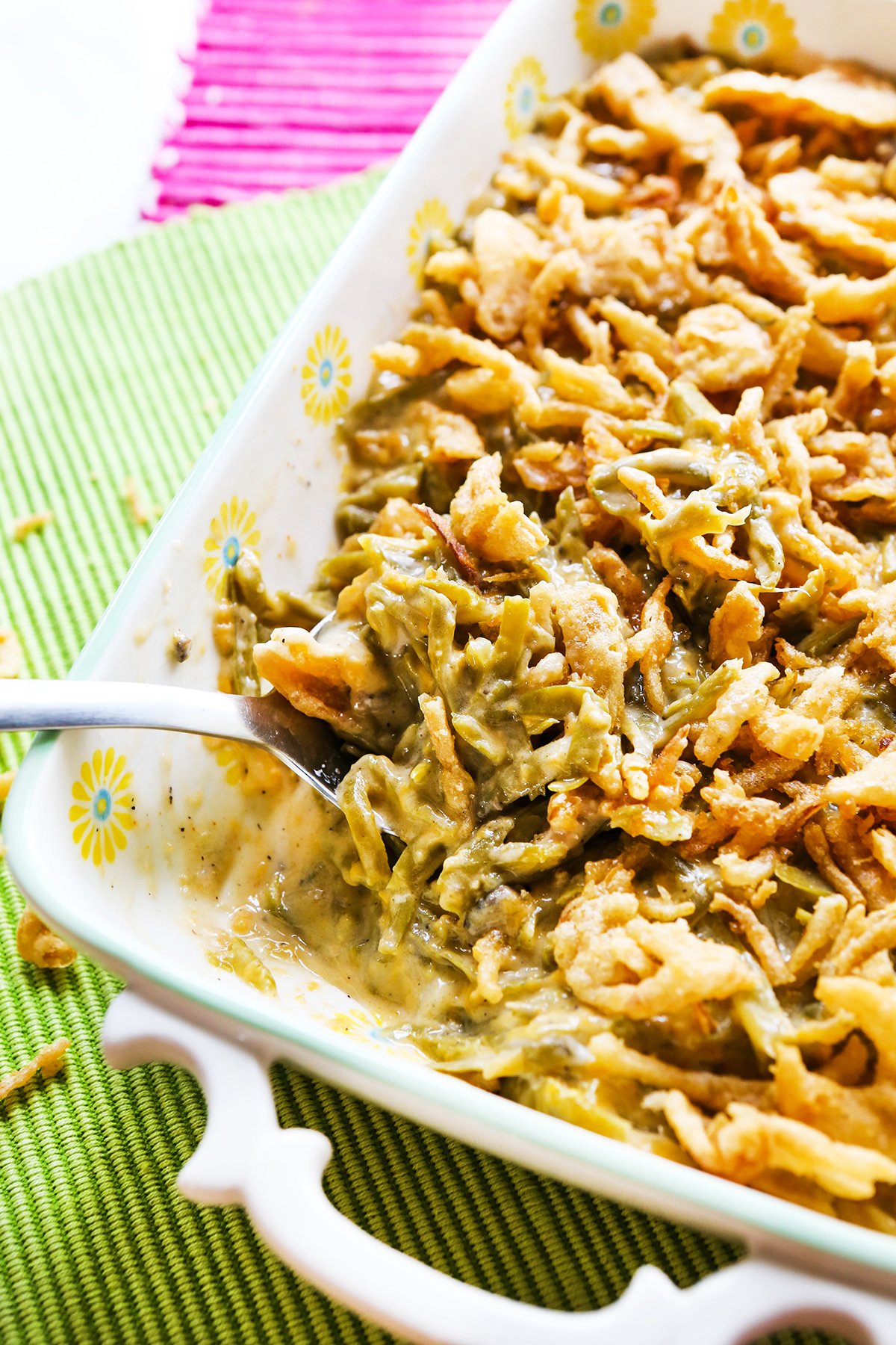 Serving spoon stuck into a dish filled with green bean casserole and crispy fried onions on top.