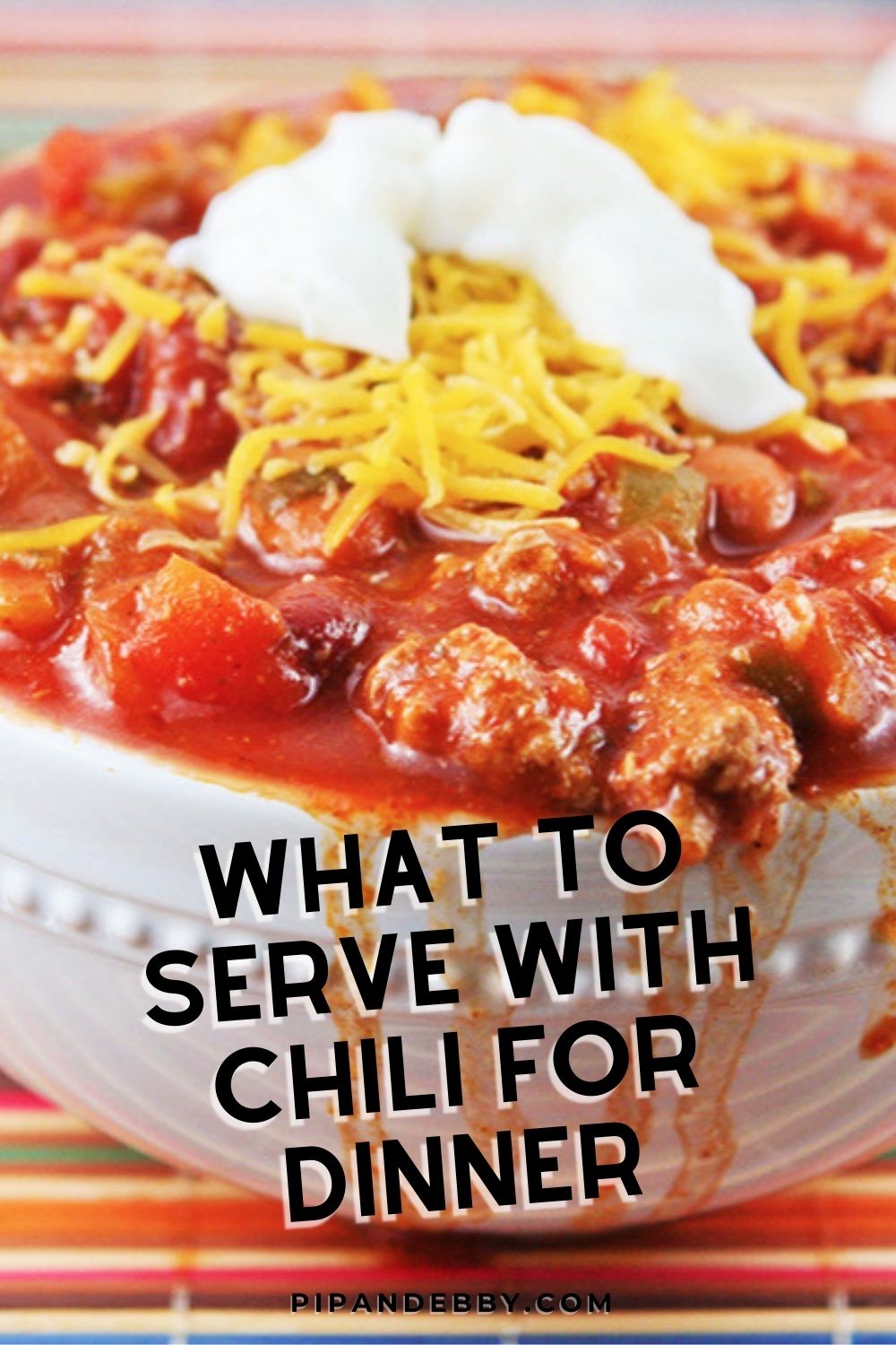 Pinterest image for what to serve with chili for dinner, a big bowl of chili with a dollop of sour cream on top