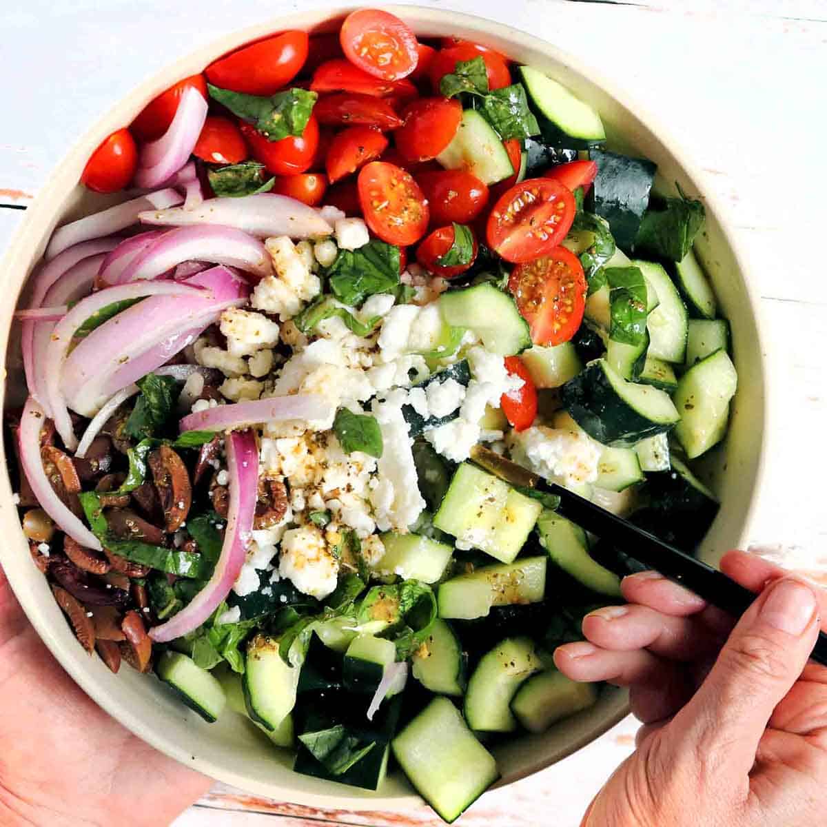 Hand scooping up some Greek cucumber salad. 