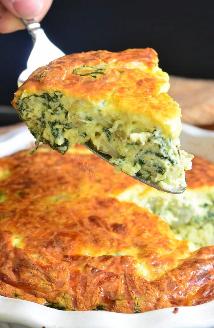 Hand serving a slice of spinach artichoke crustless quiche.