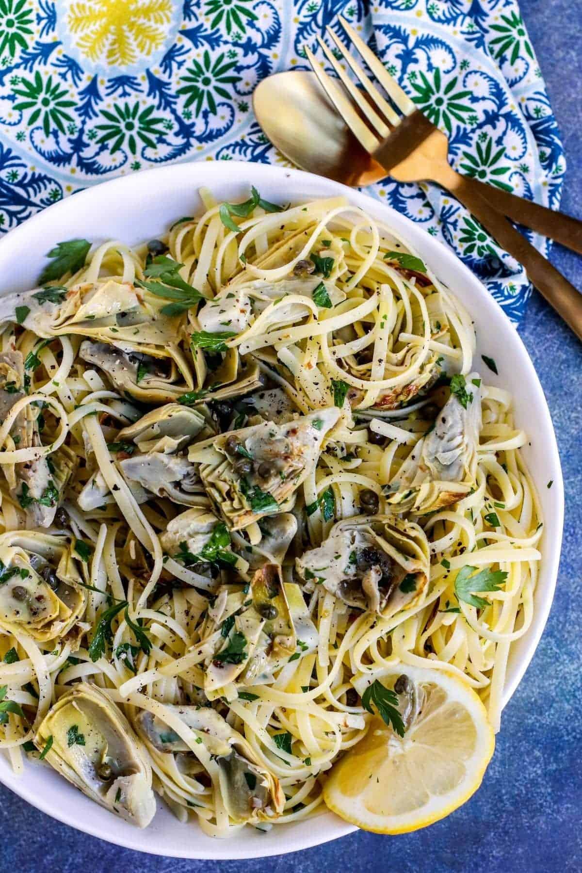 Lemon artichoke pasta in a pasta bowl garnished with a lemon slice. 