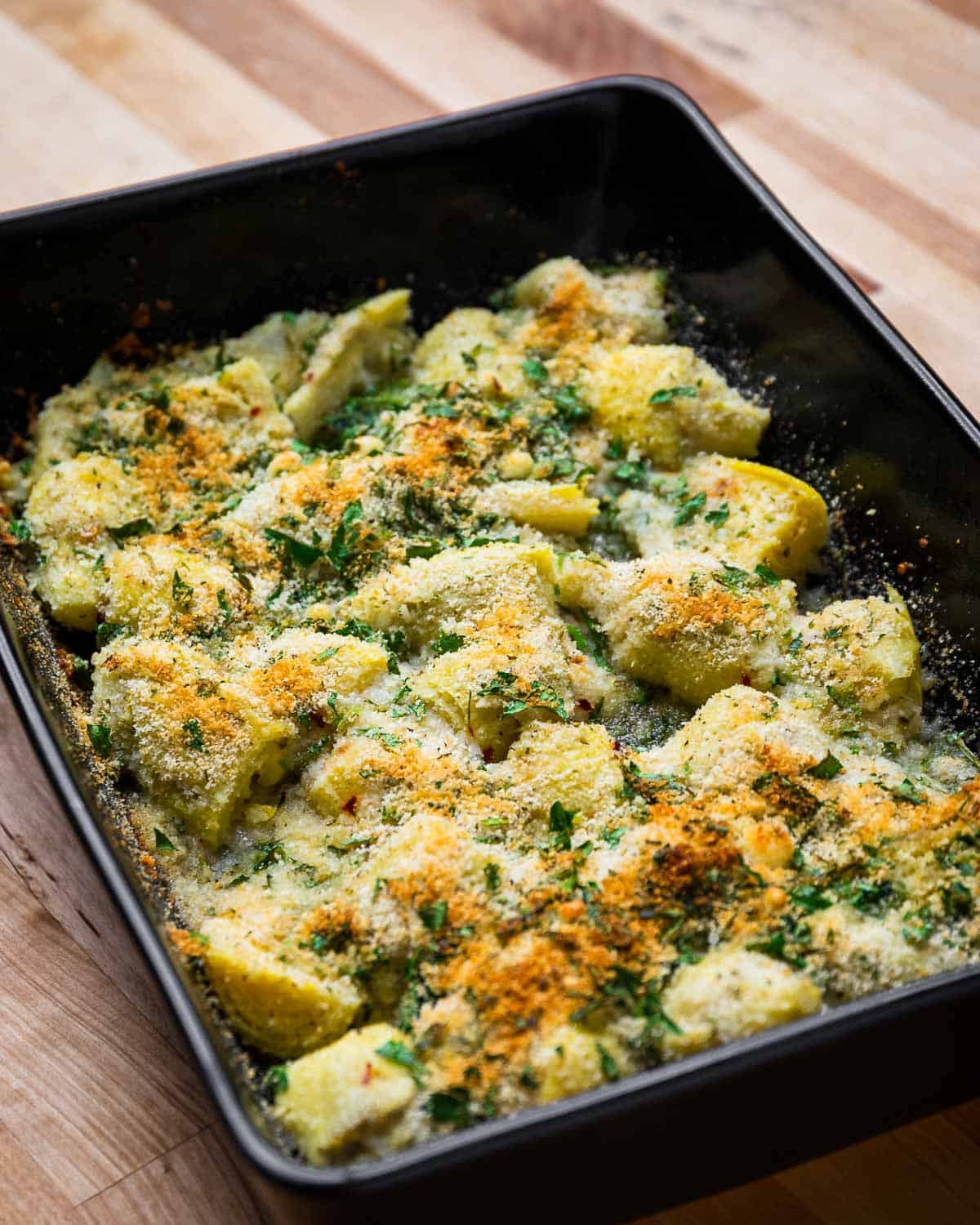 Baked artichoke hearts with seasoned breadcrumbs in a baking dish. 