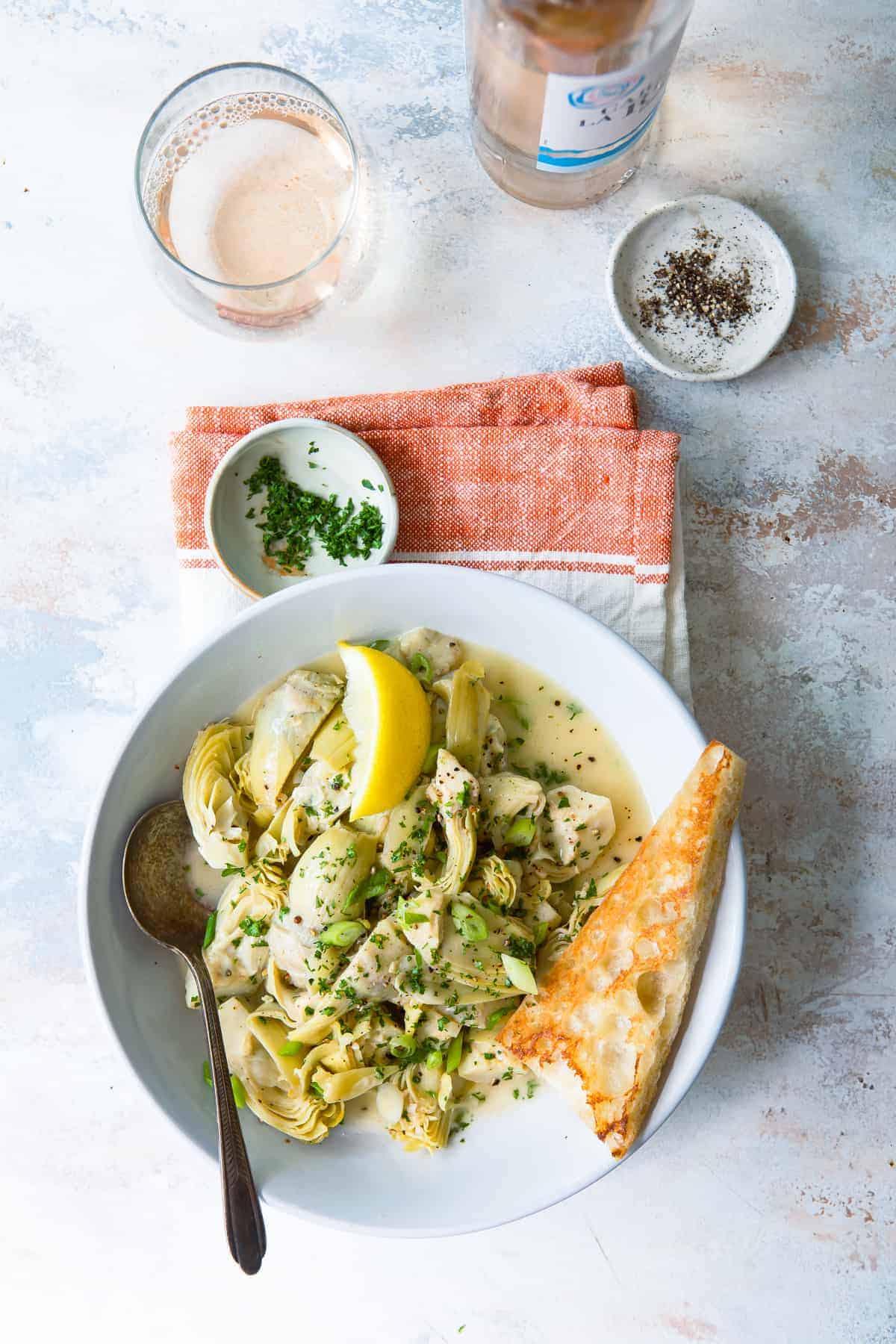 Artichoke hearts in white wine garlic and lemon sauce on a plate with garlic toast. 