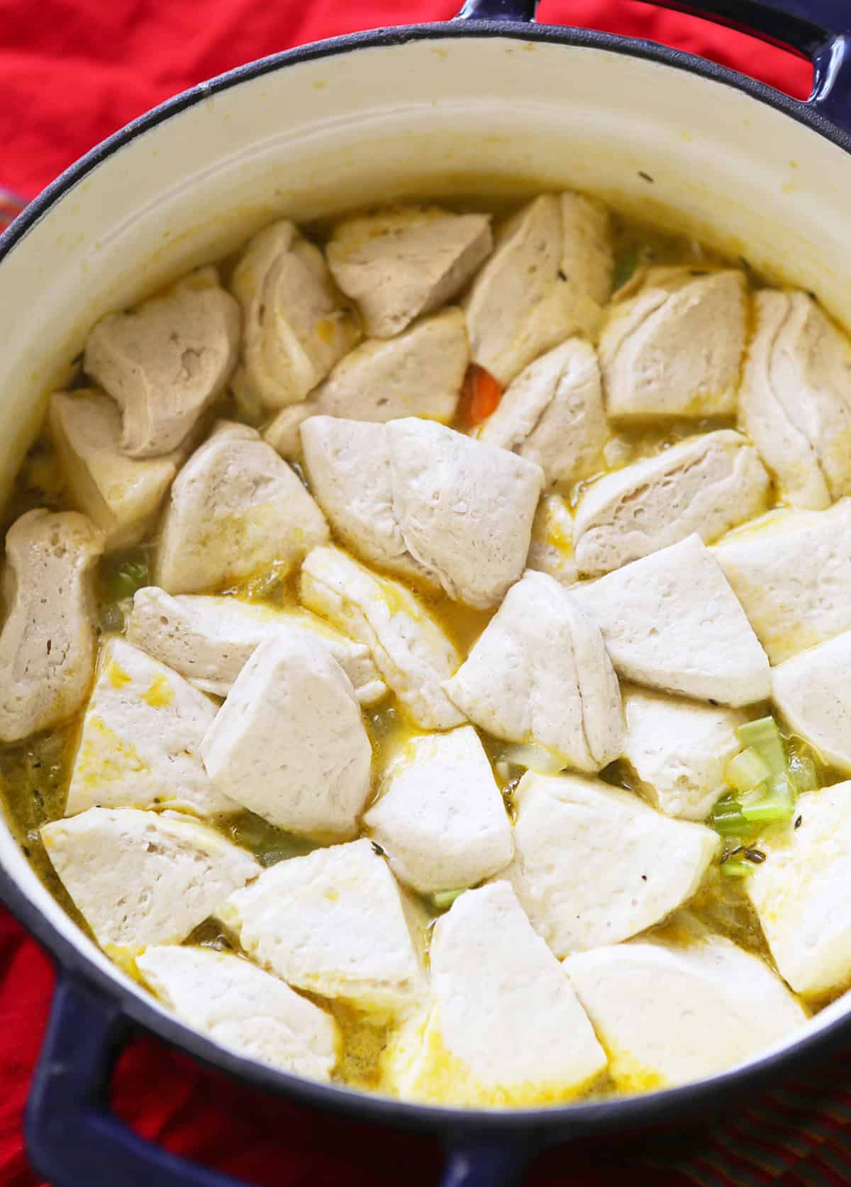 Creamy chicken and dumplings soup cooking in a pot with tender chicken pieces and vegetables.