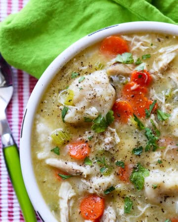 Warm chicken and dumplings soup with carrots, celery, and herbs in a white bowl.