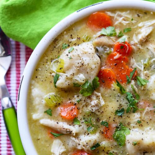Warm chicken and dumplings soup with carrots, celery, and herbs in a white bowl.