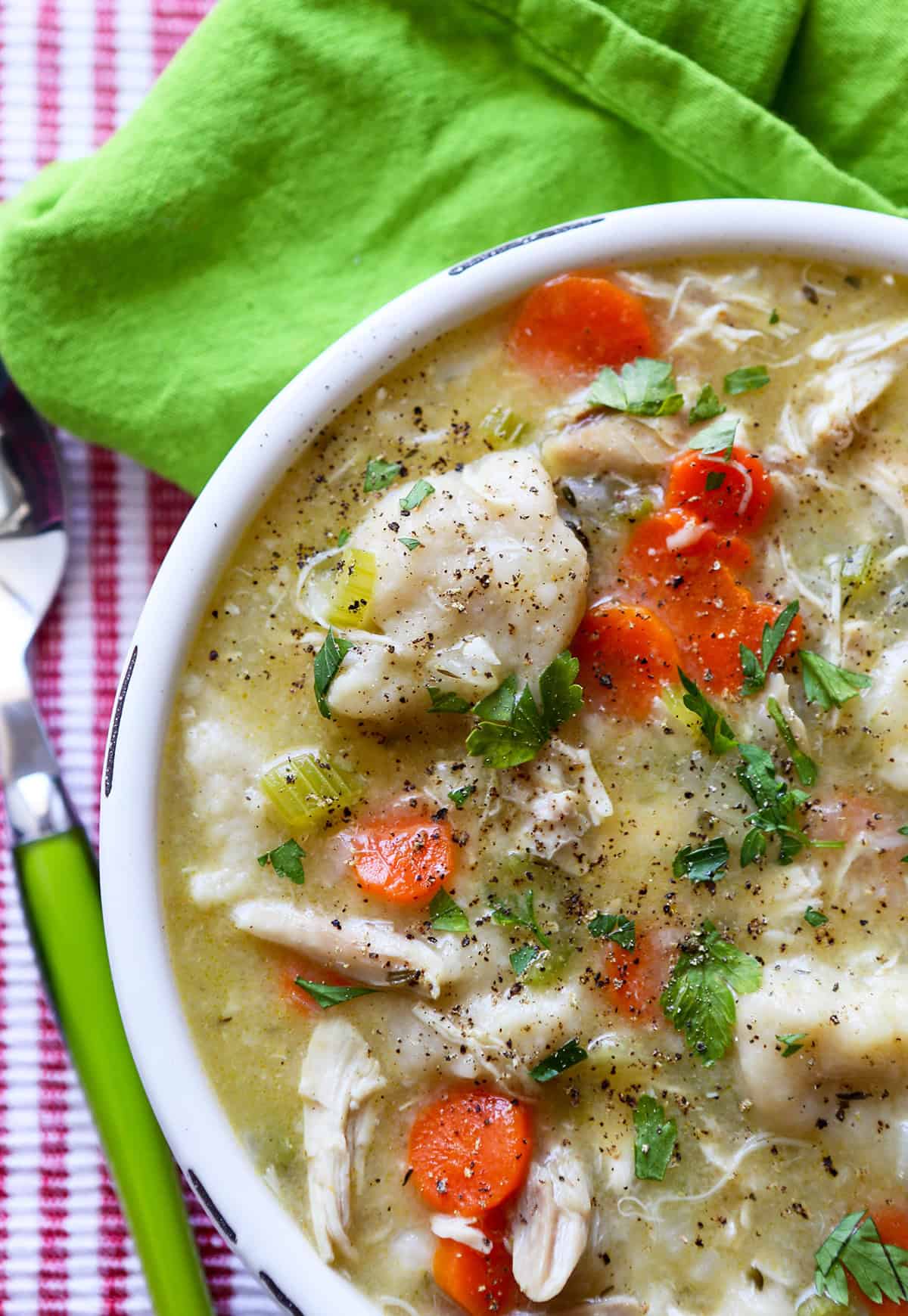 Warm chicken and vegetable soup with carrots, celery, and herbs in a white bowl.