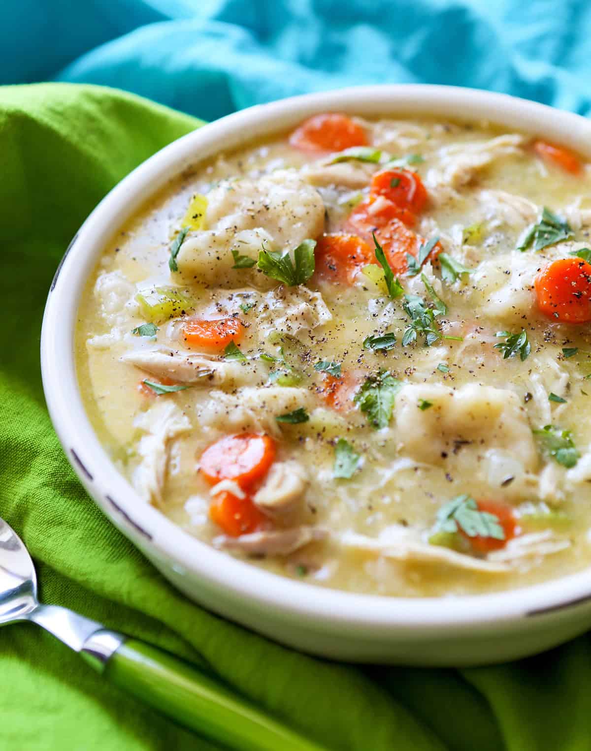 Hearty creamy chicken and vegetable soup with carrots, celery, and herbs in a white bowl.