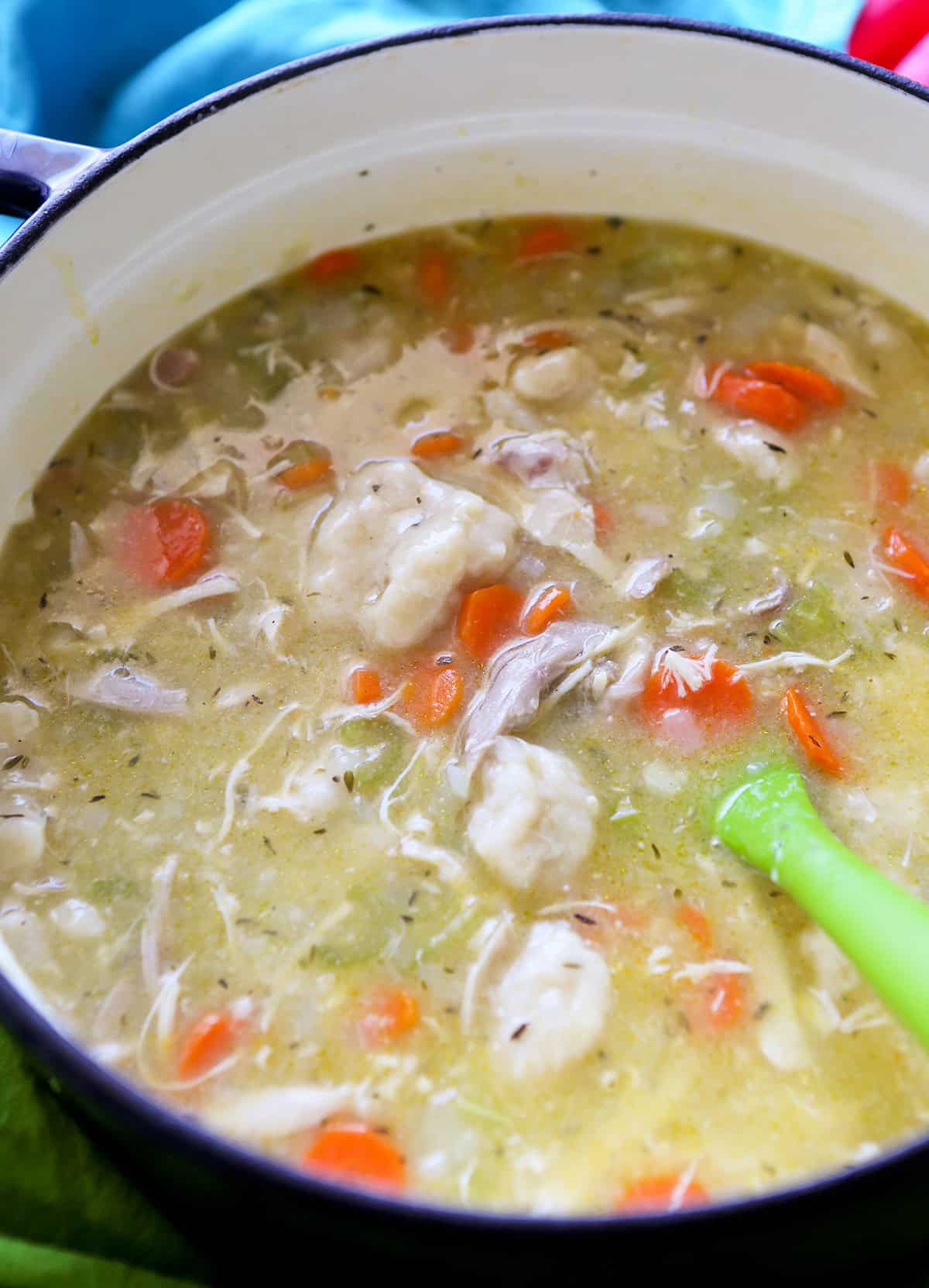 Warm homemade chicken and vegetable soup in a pot with carrots, chicken pieces, and herbs.