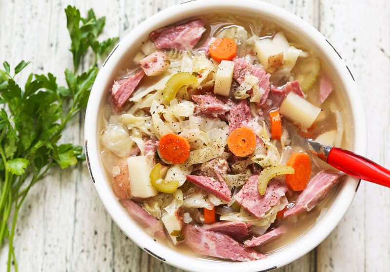 Bowl of crockpot corn beef and cabbage soup with a spoon resting in it. 