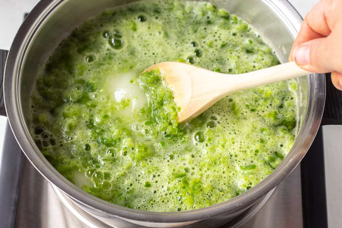 Cooking green pepper jelly in a pot with a wooden spoon.
