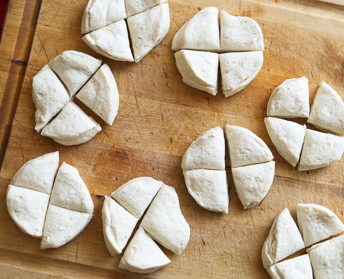Raw biscuit dough cut into rounds on a wooden surface for baking.