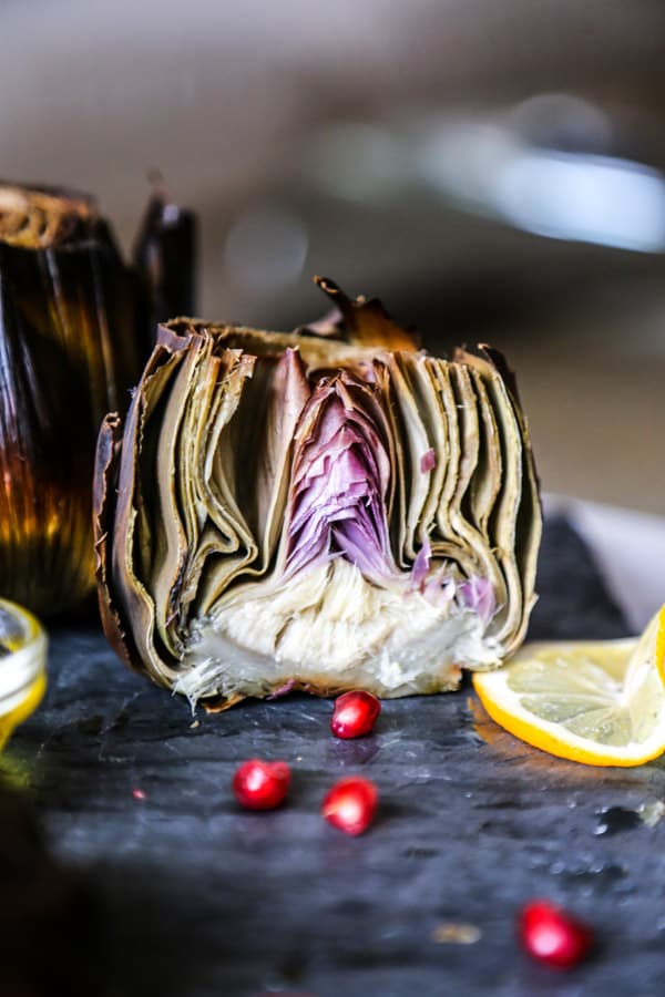 Roasted artichoke with garlic and sage next to pomegranate seeds and lemon slices. 