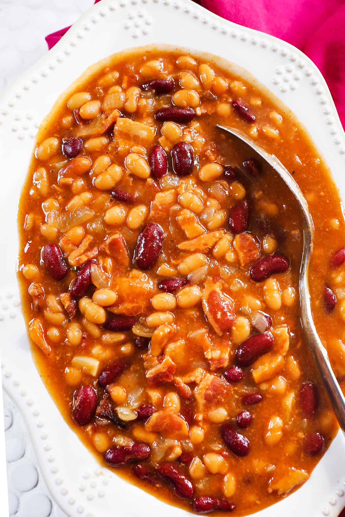 Top view of a bowl of baked beans with a serving spoon inside the mixture.