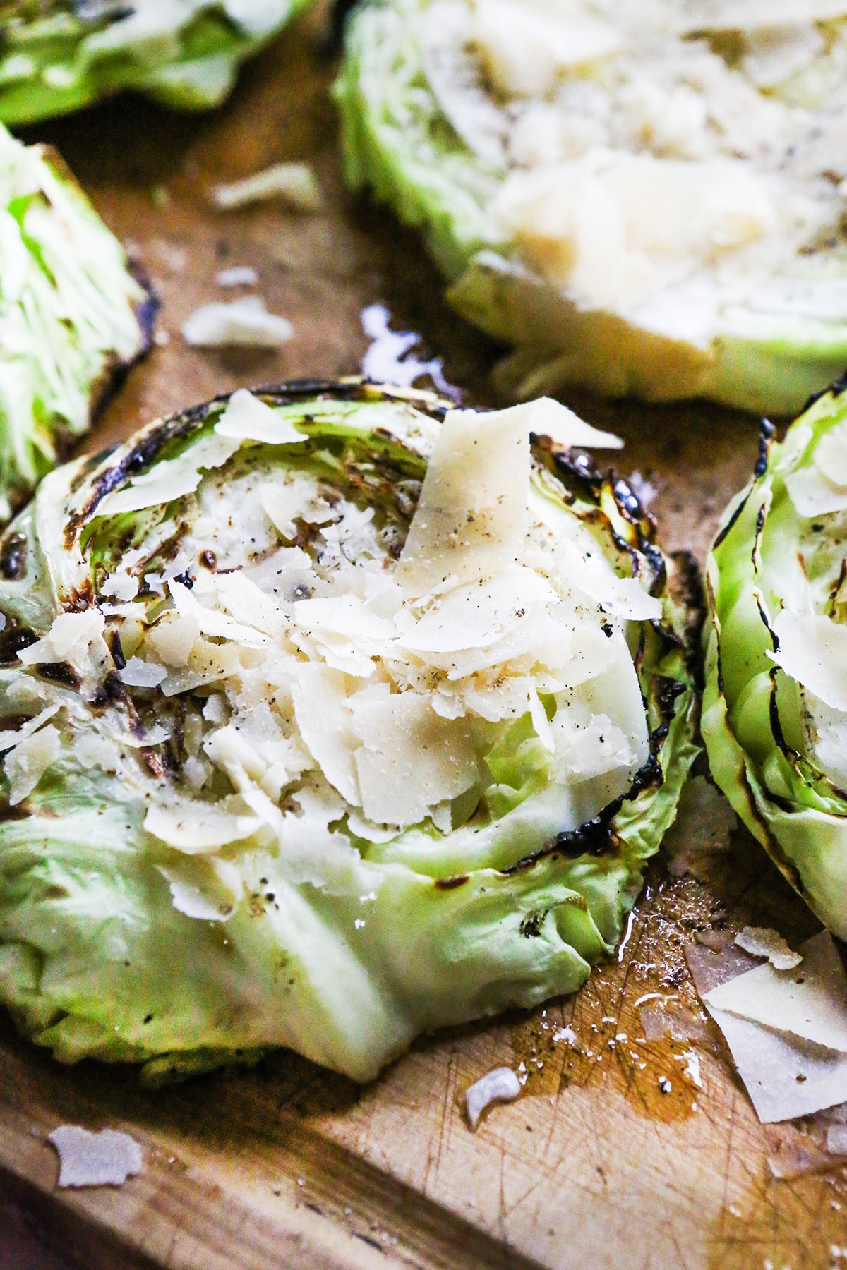 Grilled cabbage steaks on a cutting board, topped with shaved parmesan cheese and pepper.