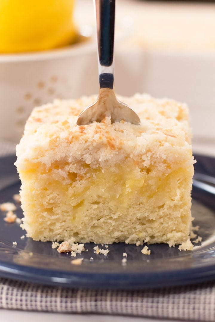 Square piece of lemon curd coffee cake with a fork stuck into the piece from the top. 